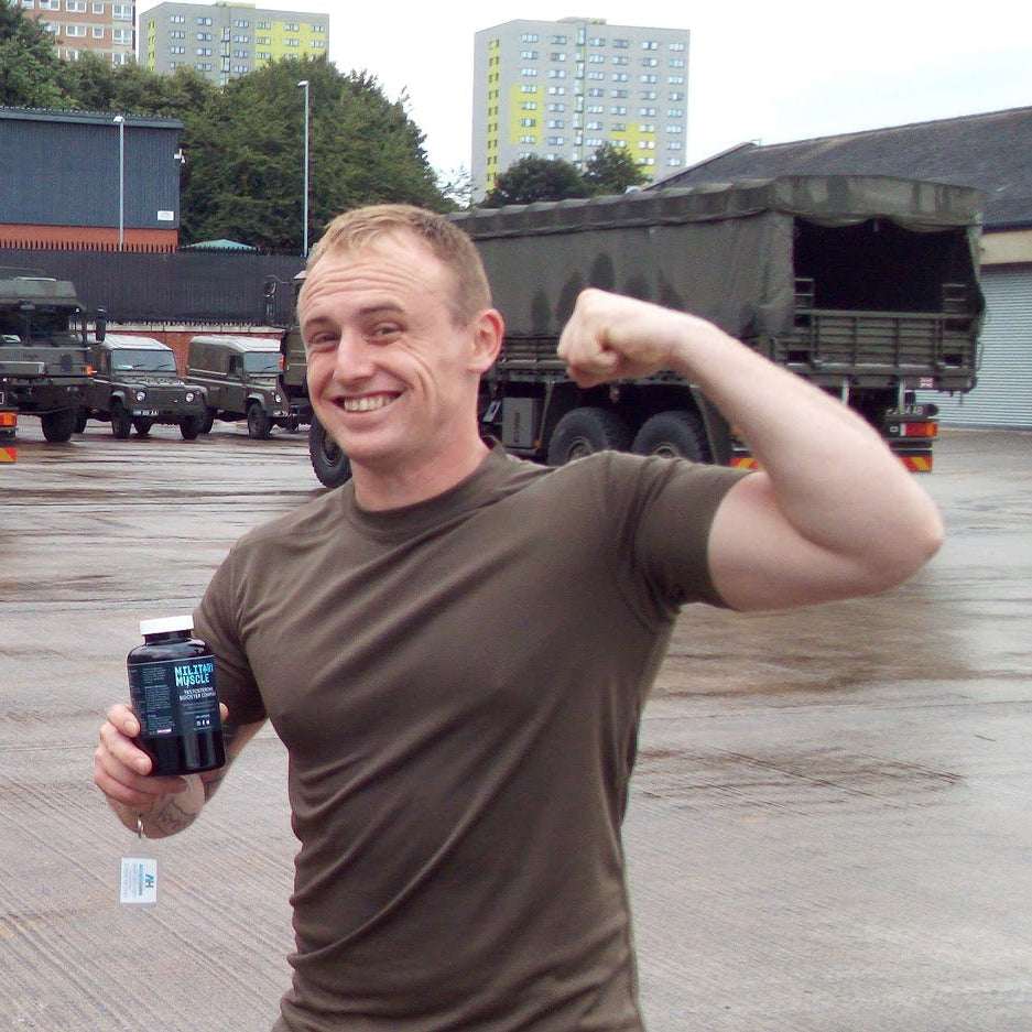 Man flexing his arm in front of military trucks in a warehouse setting