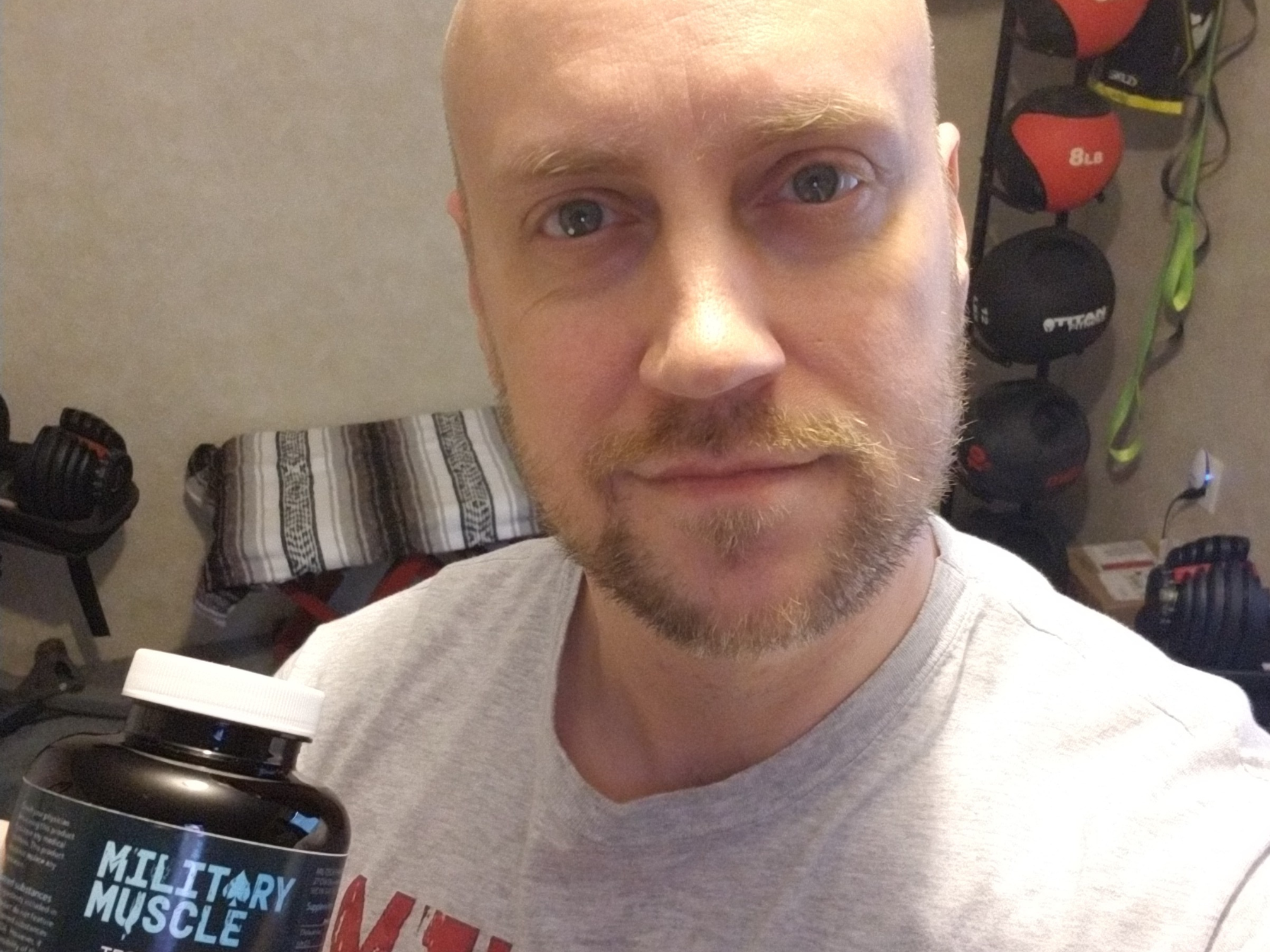 a man in a grey military muscle tee shirt holding a package of military muscle 