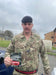 Person in military uniform holding a 'Military Muscle' product outdoors.