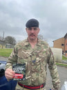 Person in military uniform holding a 'Military Muscle' product outdoors.